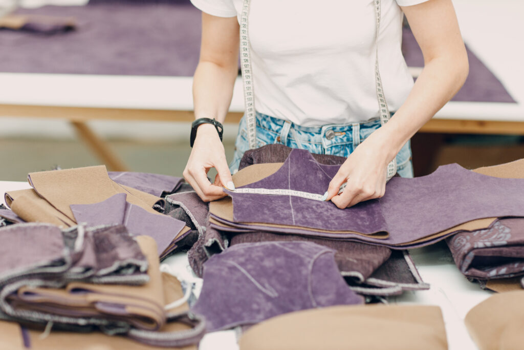 Person misst Lederstücke auf einem Arbeitstisch im Polstergeschäft.
