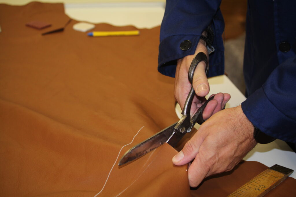 Ein Arbeiter schneidet braunen Stoff mit Scheren für Polsterarbeiten.